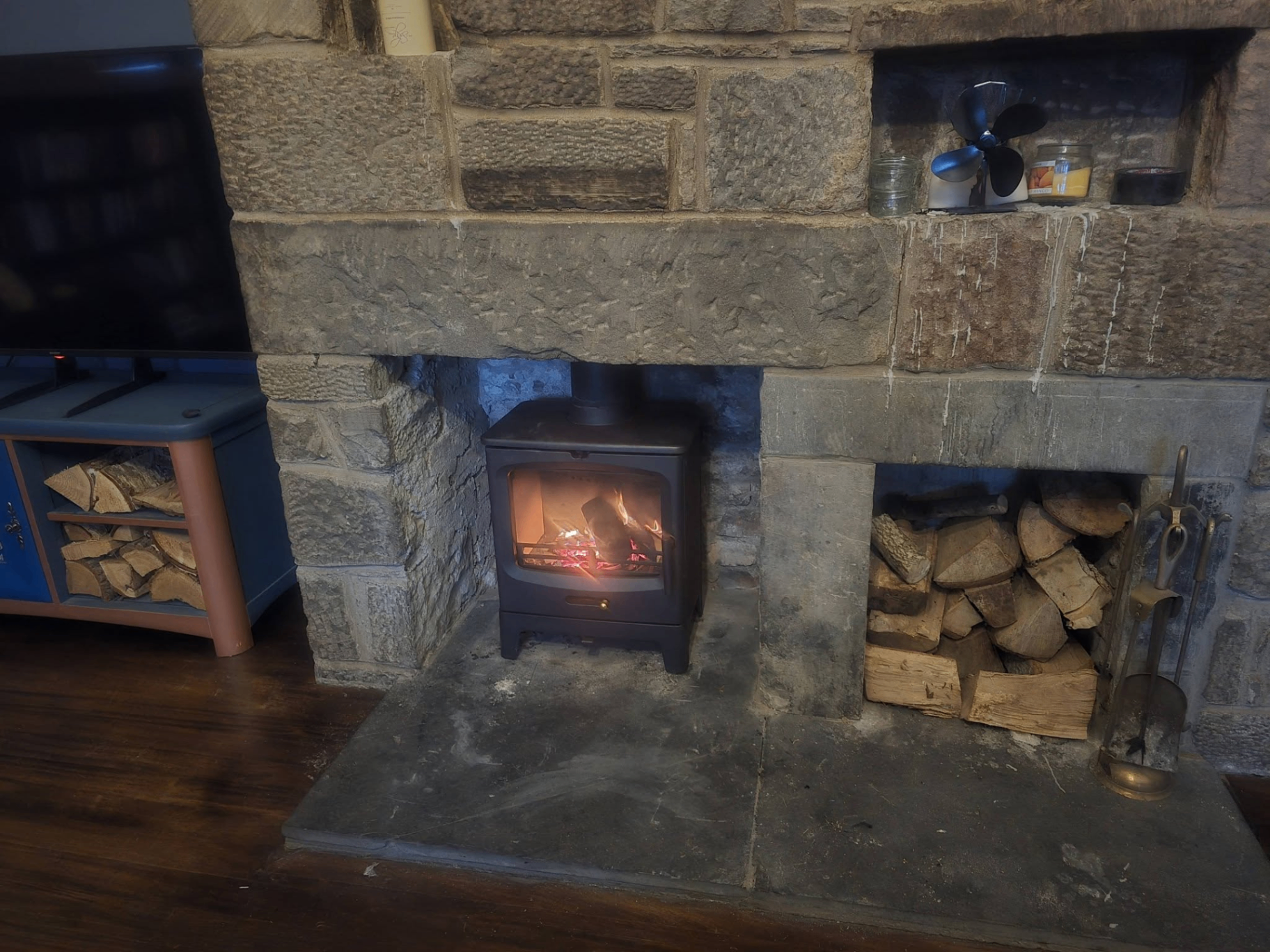 Woodburning stove in traditional stone fireplace with log store